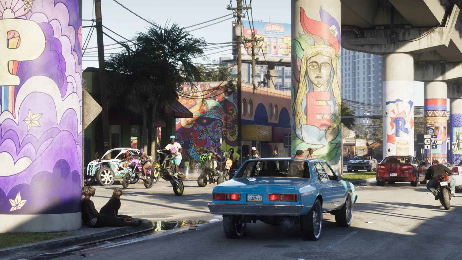 A Vice City street under an elevated highway in GTA VI: traffic queued past mural-painted support columns while riders pull wheelies on dirt bikes